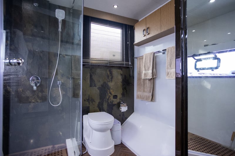 Walk-in glass shower with stone tiling and a separate toilet area.